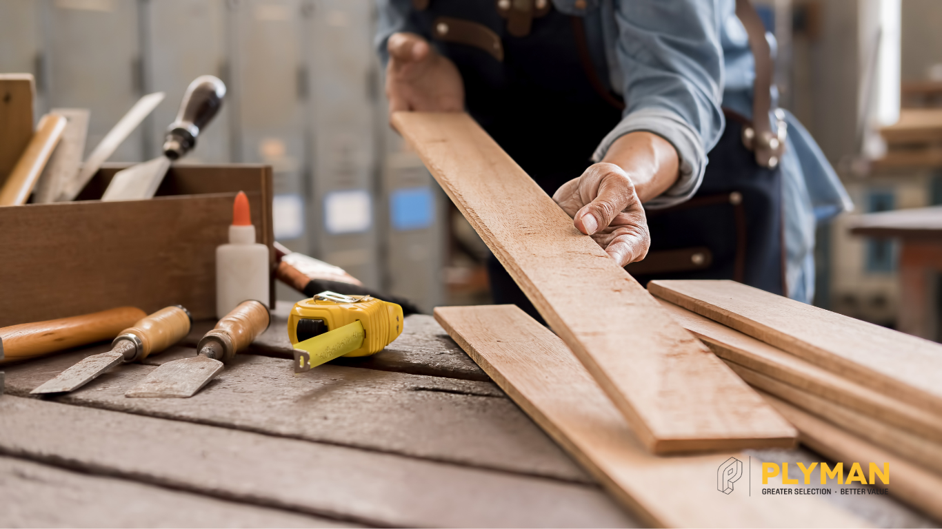 DIYer holding a plywood board at a home workshop bench